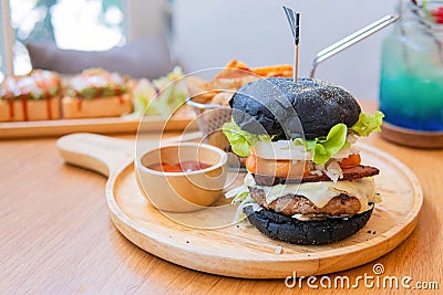 Black burger with meat patty, cheese, tomatoes, mayonnaise, french fries in a paper cup and glass of cold cola soda with ice. Stock Photo