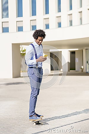 Black businessman on a skateboard looking at his smartphone outdoors. Stock Photo