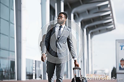 Black Businessman Traveler Walking With Suitcase Near Rail Station Outdoors Stock Photo