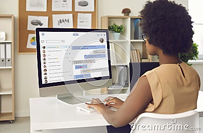 Black businesswoman sitting at office desk and messaging colleagues on work chat Stock Photo