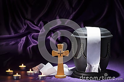 Black cemetery urnk with cross and candles and white ribbon on deep purple background Stock Photo