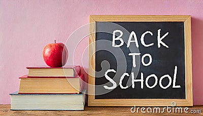 Black chalkboard, books and apple on light pink background Stock Photo