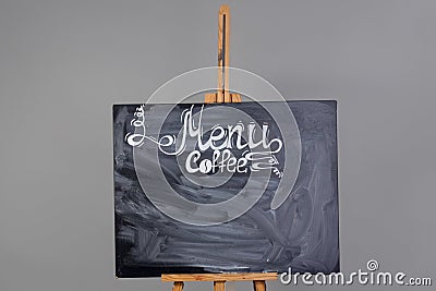 Black chalkboard with coffee menu and streaks of erased chalk. Stands on wooden easel, isolated on a gray background Stock Photo