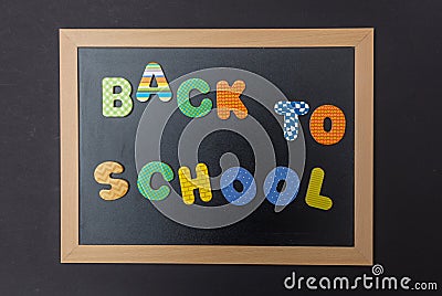 Black chalkboard with wooden frame, text back to school in colorful letters, black wall background Stock Photo