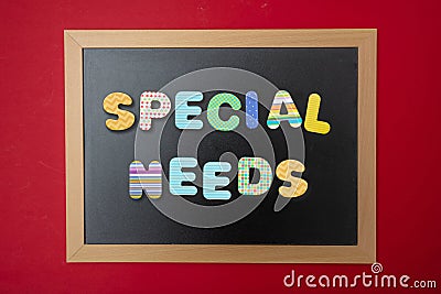 Black chalkboard with wooden frame, text special needs in colorful letters, red wall background Stock Photo