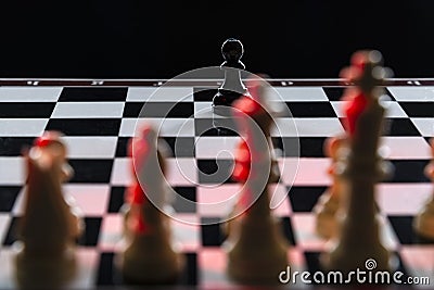 Black chess pawn against an army of white chess pieces on a chessboard on a black background Stock Photo