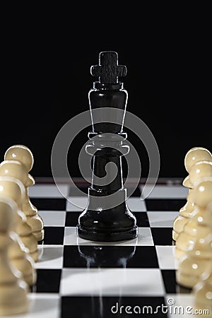 Black chess queen and army of white pawns on a chessboard on a black background Stock Photo