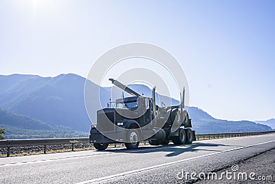 Black classic big rig semi truck with semi trailer for transportation wood logs running on the road along Columbia River in Stock Photo