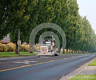 Black classic bonnet big rig semi truck with vertical pipes going on divided road with green trees Stock Photo