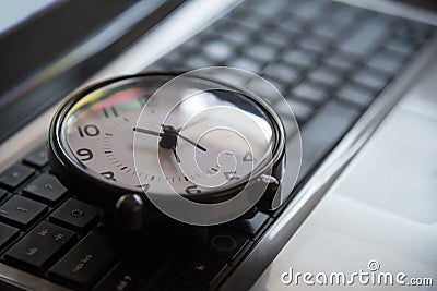 Black clock lay on keyboard time metaphor concept in dark low key tone, selective focus. Stock Photo