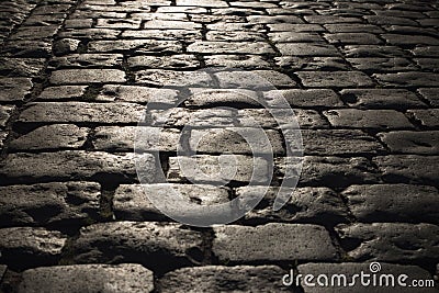 Black cobbled stone road background with reflection of light seen on the road. Black or dark grey stone pavement texture. Stock Photo