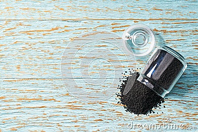 black cumin are poured from a glass jar on a blue wooden background, with copy space. Top view Stock Photo