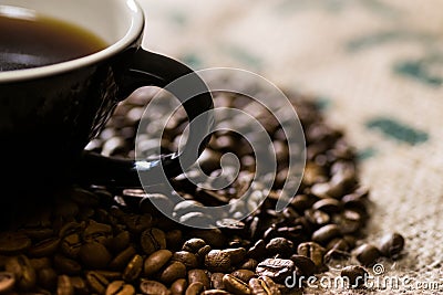 Black cup with handle, on a coffee sack with roasted beans around Stock Photo