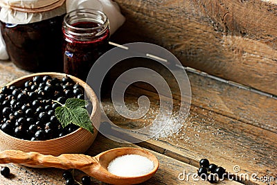 black currant berries in a wooden dish on a wooden table with a jar of jam, a wooden spoon with sugar, concatenation of Stock Photo