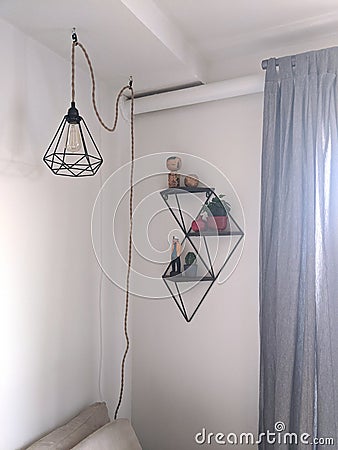 Black designer geometric lamp hanging on a cord with shelves on a wall and curtains Stock Photo