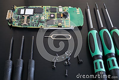 Black desk with disassembled cellphone, screws, screwdrivers ready for repairing Stock Photo