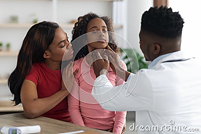 Black doctor palpating school girl throat at clinic Stock Photo