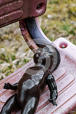 Black doll lying on dirty swing at abandoned playground Stock Photo