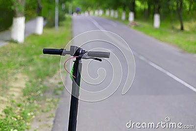 Black electric scooter transport is parked along the road of the park on sunny summer day. Eco alternative transport Stock Photo