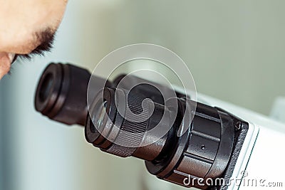 The man`s eye is looking through the microscope. Black eyepieces of professional laboratory magnifying equipment close-up. Stock Photo