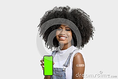 Black girl without face shield holds the cell phone close to her arm with the vaccine sticker, fully immunized, chroma key on the Stock Photo