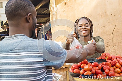 black girl selling tomatoes in a local african market to a customer smiling and feeling happy and satisfied Stock Photo
