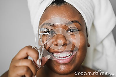 Black girl using eyelash curler while wearing body towel - Main focus on eyes Stock Photo