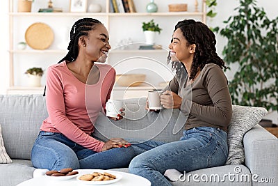 Black girlfriends enjoying weekend together, drinking coffee on couch Stock Photo