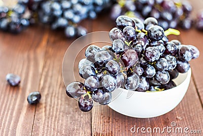 Black grape branch in bowl on dark wooden background Stock Photo