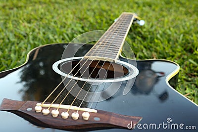 Black guitar lying on the green lawn with a focus on the strings Stock Photo