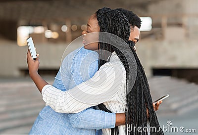 Black guy and girl hugging but looking at smartphones over shoulder Stock Photo