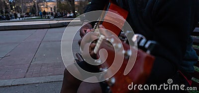 Black guy playing a guitar and singing happy sitting in a bench of a park Stock Photo