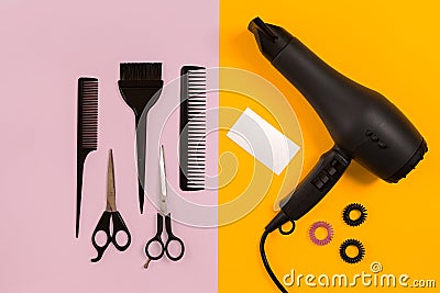 Black hair dryer, comb and scissors on pink and yellow paper background. Top view Stock Photo