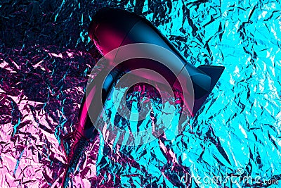 Black hair dryer in neon lights on the foil with shiny crumpled surface background. Stock Photo