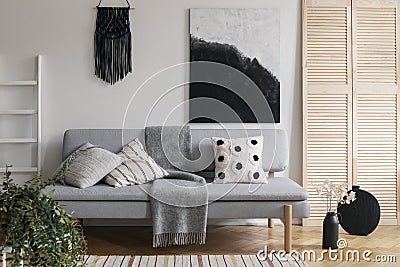 Black handmade macrame and fancy painting on white wall of sophisticated living room interior with grey fashionable couch with Stock Photo