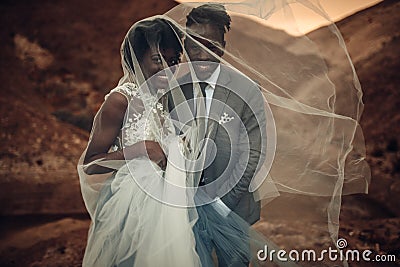 Newlyweds stand under bridal veil and smile in canyon at sunset. Stock Photo