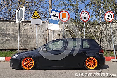 Black hatchback with orange wide wheels tuned by air suspencion parked under different road signs Stock Photo