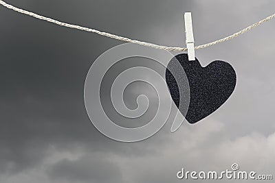 Black Heart paper hanging on a brown hemp rope on rain clouds ba Stock Photo