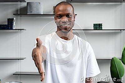 Black HR agent, a male recruiter, reaches out to the camera for a handshake, greeting the candidate, showing a polite Stock Photo