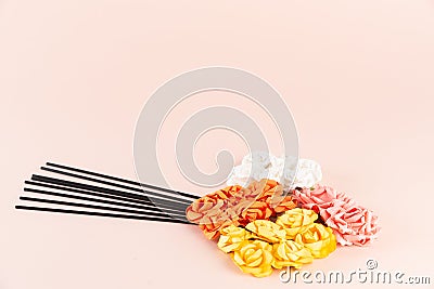 Black incense sticks with white, pink, orange and yellow flowers on pink background Stock Photo