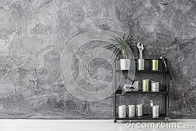 Black industrial shelf with cans, tools and plant on grey concrete wall Stock Photo