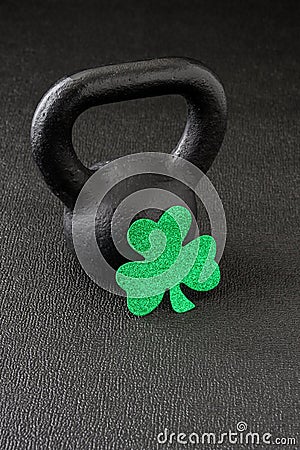 Black iron kettlebell and green glitter shamrock on a black gym floor, happy St. Patrick’s Day Stock Photo