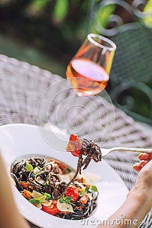 Black italian pasta with tomato sauce and parmesan, served on white plate with glass of wine, product photography for restaurant Stock Photo