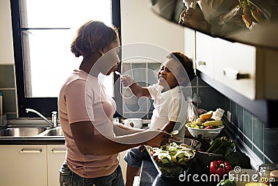 Black kid feeding mother with cooking food in the kitchen Stock Photo