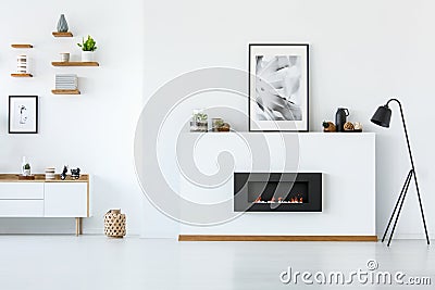 Black lamp next to fireplace under posters in minimal white living room interior. Real photo Stock Photo