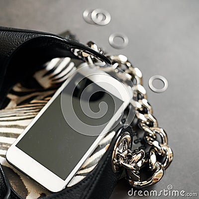 Black leather bag with chain, white phone, zebra print, silver thin rings on a black background. Top view. Copy space Stock Photo