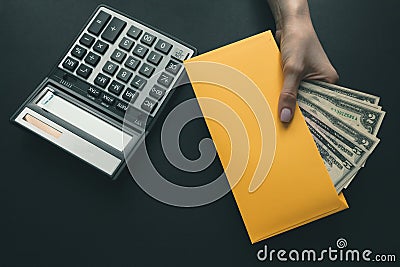 On the black leather desk a calculator, the girl holds in her hand a yellow envelope with money, salary for work Stock Photo