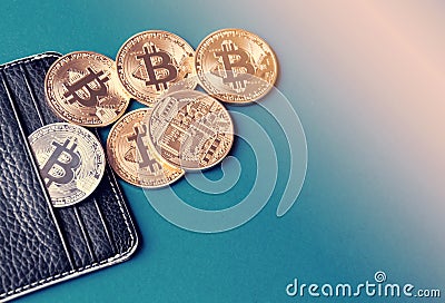 Black leather wallet on a blue background with several gold and silver coins of bitcoins falling out of their pockets. Stock Photo