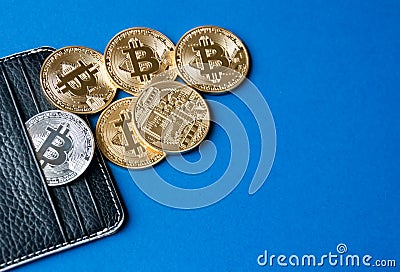 Black leather wallet on a blue background with several gold and silver coins of bitcoins falling out of their pockets. Stock Photo