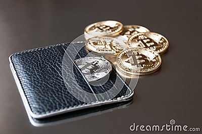 The black leather wallet on a dark background with several gold and silver coins of bitcoins falling out of their pockets. Stock Photo